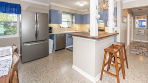 A modern kitchen with a stainless steel refrigerator, blue cabinets, a wooden island with stools, and a view of the outdoors. - Tropical oasis (Lake Worth)