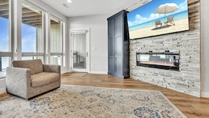 Ein Wohnzimmer mit Kamin, großem Fenster und einem Gemälde zum Thema Strand.