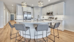 A modern kitchen with white cabinets, stainless steel appliances, and a central island with bar stools. - Waters Edge in the Stillwater at Bridges Bay Resort (Arnolds Park)