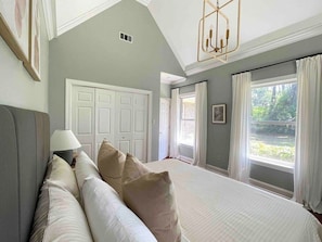 A bedroom with a large bed, a nightstand, a lamp, a wardrobe, and a window with curtains.
