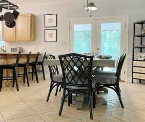 Een eetruimte met een tafel en stoelen, een keuken met kasten, en uitzicht door een deur.
