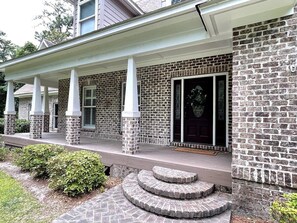 A brick house with a porch, a front door, and a staircase leading to the entrance.