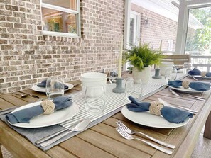 Een eettafel gedekt met borden, glazen, bestek en servetten, met een bakstenen muur en een raam op de achtergrond.