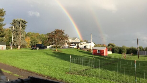 A rural landscape with a rainbow, houses, and a fenced field.