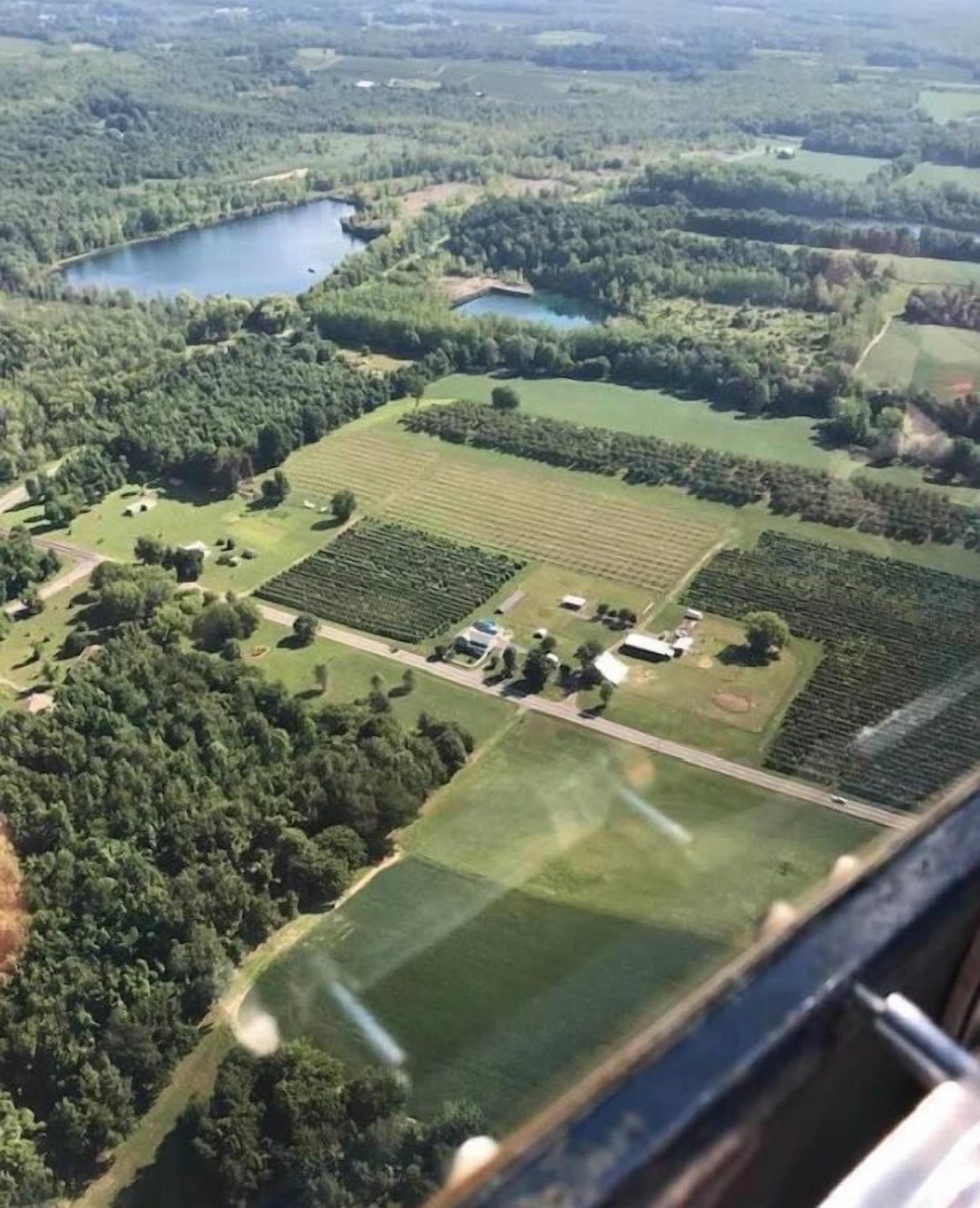 Une vue aérienne d’un paysage rural, avec des champs, un lac et de vastes zones boisées.
