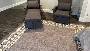 A room with two dark gray recliner sofas, a patterned rug, and a painting on the wall.