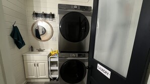 A laundry room with two stacked front-loading washers and dryers, a small sink with a mirror, and a towel rack. - Reel Life Lakehouse - Boat Ramp in Neighborhood (Broaddus)