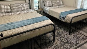 Two single beds with metal frames, a small bedside table with a lamp, and a patterned rug on a wooden floor. - Reel Life Lakehouse - Boat Ramp in Neighborhood (Broaddus)