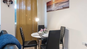 Un comedor con una mesa dispuesta para cuatro, sillas negras, un cráneo decorativo en la pared y una pintura de atardecer.