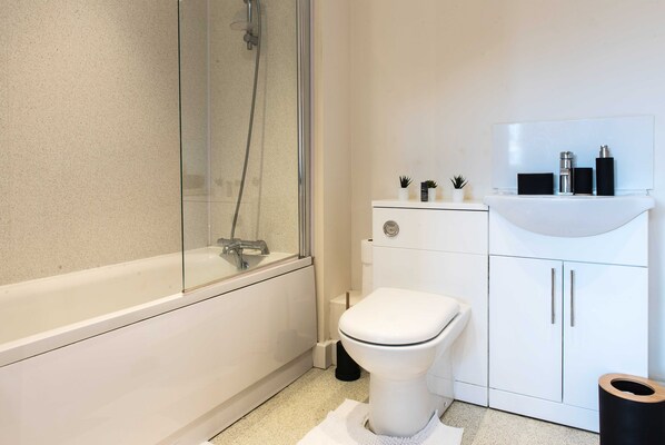 A modern bathroom with a glass-enclosed shower, a white toilet, and a sink with a mirror above it.