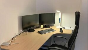 Ein Büro im Eck mit Schreibtisch, zwei Monitoren, Tastatur, Stuhl und einer Schreibtischlampe.