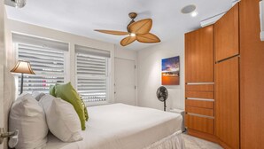 A bedroom with a bed, a ceiling fan, a wall-mounted fan, and a wooden wardrobe.