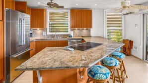 A modern kitchen with a central island, stainless steel appliances, wooden cabinets, and a ceiling fan.