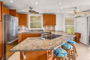 A modern kitchen with a central island, stainless steel appliances, wooden cabinets, and a ceiling fan.
