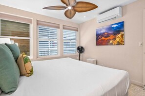 Un dormitorio con una cama, ventilador de techo, aire acondicionado y un cuadro en la pared.