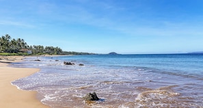 Ein Strand mit blauem Himmel, ruhigem Wasser und einem entfernten Berg.