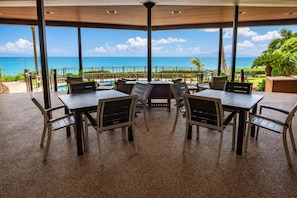 A covered outdoor seating area with tables and chairs, overlooking a pool and the ocean.