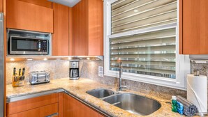A kitchen with wooden cabinets, a stainless steel sink, a microwave, a toaster, and a coffee maker.