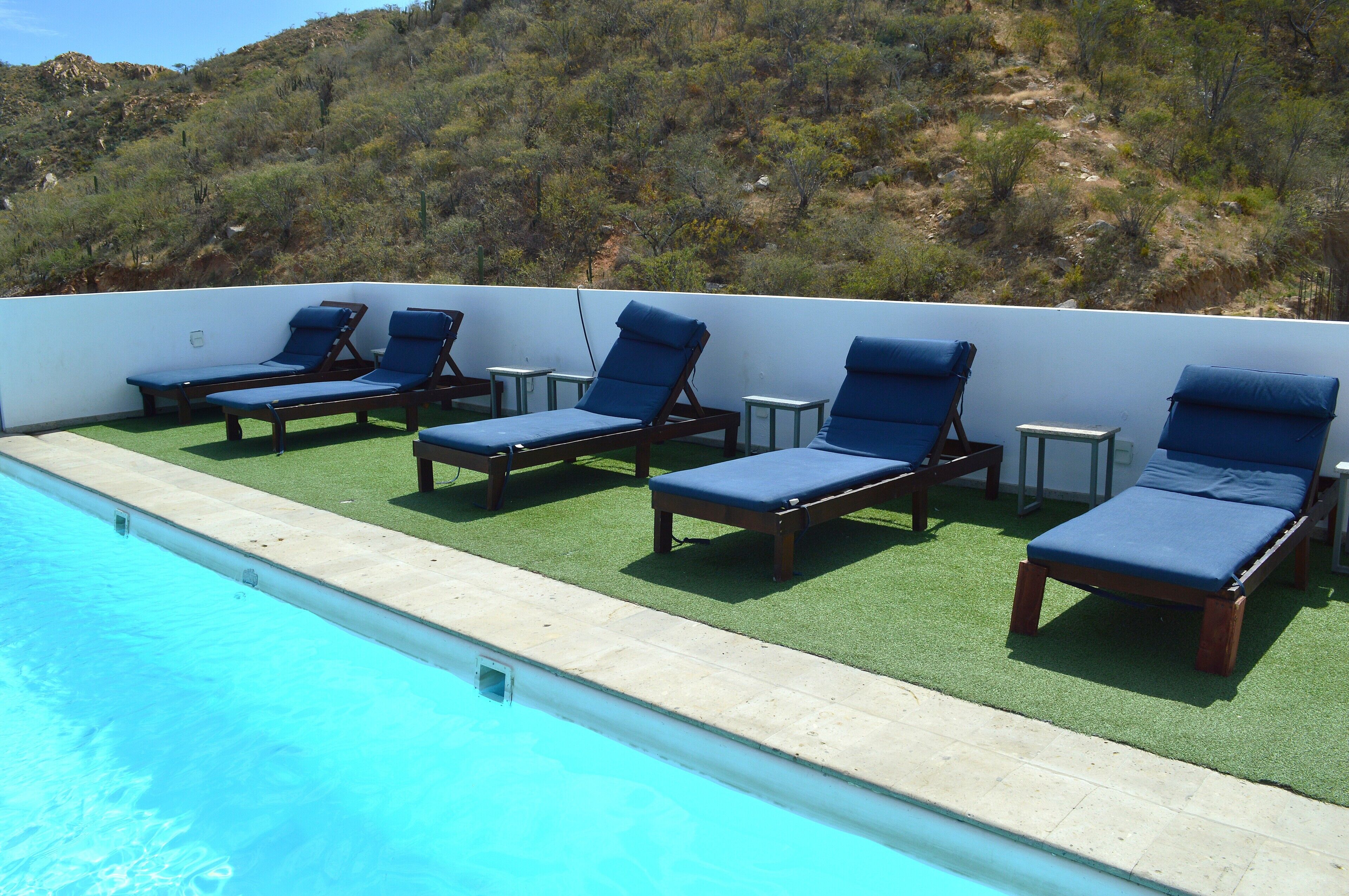 A poolside area with lounge chairs and a view of a hilly landscape.