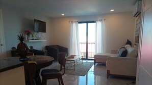 Ein modernes Wohnzimmer mit Essbereich, einer Couch, einem an der Wand montierten Fernseher und einem Balkon mit Vorhängen.