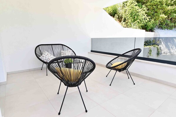 A modern outdoor seating area with three black wireframe chairs and a white wall.