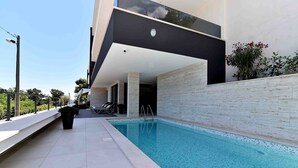 A modern outdoor pool area with a clear blue pool, a tiled deck, and a black and white building with a balcony.