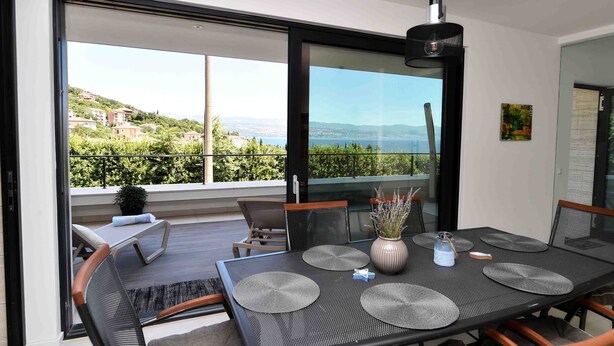 A modern dining area with a large table, chairs, and a view of a hillside.