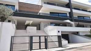 A modern multi-story building with a prominent staircase leading to the entrance, large windows, and a gated driveway.