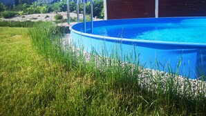An outdoor swimming pool with a metal ladder, surrounded by grass and rocks. - Cozy vacation cabin in the middle of the Lusatian Lakeland (Lauta)