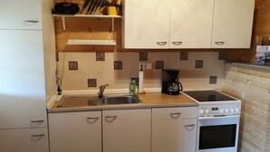 A compact kitchen with white cabinets, a sink, a stove, and a coffee maker. - Cozy vacation cabin in the middle of the Lusatian Lakeland (Lauta)