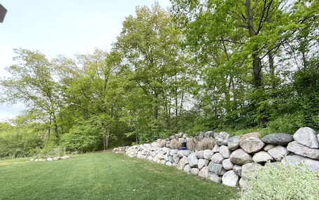 A landscaped garden with a stone wall, green grass, and trees.
