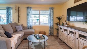 A living room with a sofa, a glass coffee table, a TV, and a window with curtains.