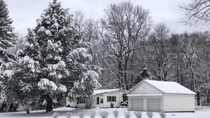 Ein mit Schnee bedecktes Haus mit Garage und einem großen Baum im Vordergrund.