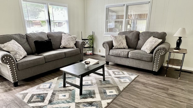 Ein Wohnzimmer mit zwei grauen Sofas, einem Couchtisch und einem gemusterten Teppich.