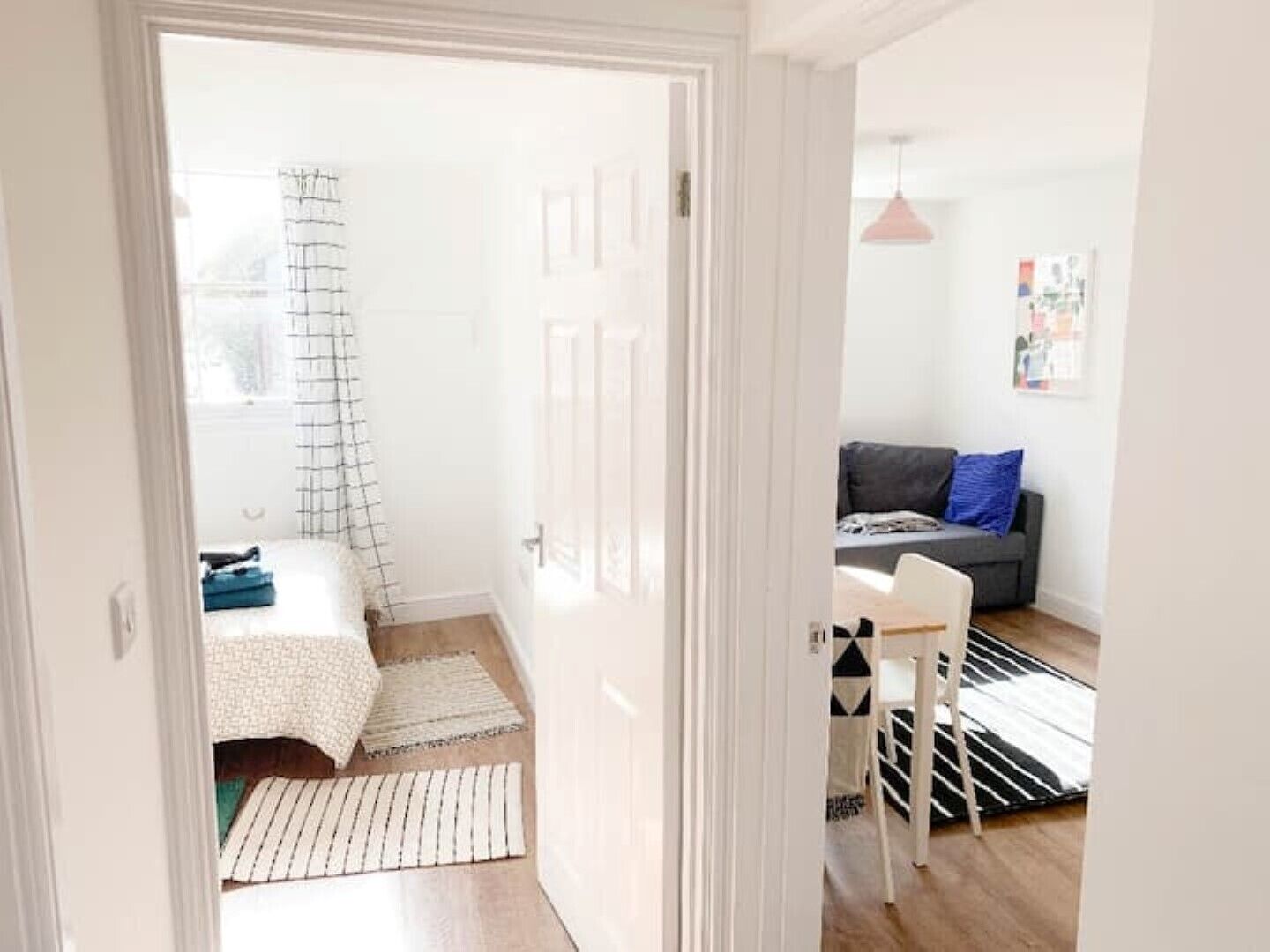 A room with a bed, a grey sofa, a black and white striped rug, and a hanging pendant light.