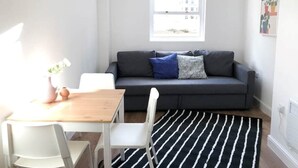 Una sala de estar moderna con un sofá gris, sillas blancas, una mesa de madera y un tapete a rayas blanco y negro.