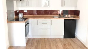 Una cocina compacta con gabinetes blancos, una campana extractora de acero inoxidable, una cafetera y un lavavajillas.