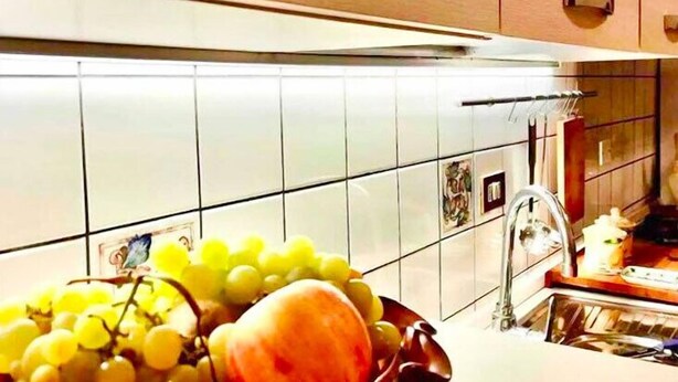 A kitchen with white tiled backsplash, a sink, and a bowl of fruit on the counter.