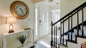 Un couloir avec une horloge murale, une lampe, un vase de fleurs et un escalier.