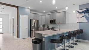 A modern kitchen with a central island, bar stools, stainless steel appliances, and pendant lighting.