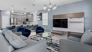 A modern living room with grey sofas, a glass coffee table, and a TV mounted on the wall.
