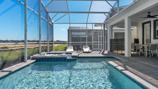 A swimming pool with a glass enclosure, a hot tub, and a patio area with chairs and tables.