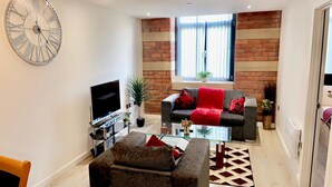 A modern living room with a flat-screen TV, a glass coffee table, and a sofa with red cushions. - Charming 1-bed Apartment in Bradford City Holiday (Bradford)