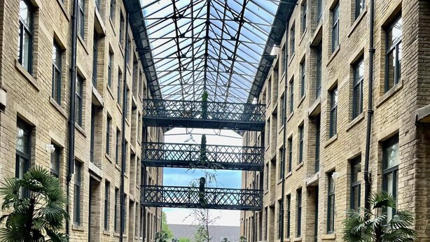 A covered courtyard with a central pathway, surrounded by brick buildings and potted plants. - Charming 1-bed Apartment in Bradford City Holiday (Bradford)