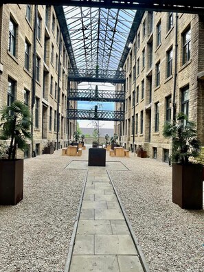 A covered courtyard with a central pathway, surrounded by brick buildings and potted plants. - Charming 1-bed Apartment in Bradford City Holiday (Bradford)