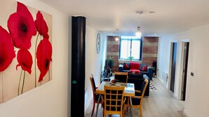 A modern living room with a sofa, coffee table, and chairs. There is a dining area with a table and chairs. The room has a brick wall and a window with curtains. - Charming 1-bed Apartment in Bradford City Holiday (Bradford)