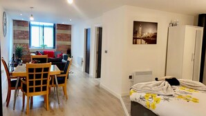 A modern apartment with a dining area, a living room with a sofa and a coffee table, a bed with a floral duvet, and a painting of a cityscape. - Charming 1-bed Apartment in Bradford City Holiday (Bradford)