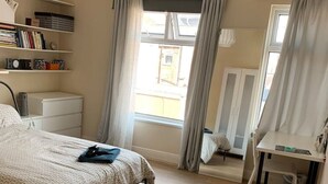 Une chambre à coucher comprenant un lit, un bureau, une chaise, une armoire et une fenêtre avec des rideaux.