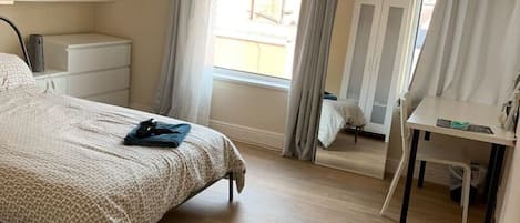 A bedroom with a bed, a desk, a chair, a wardrobe, and a window with curtains.