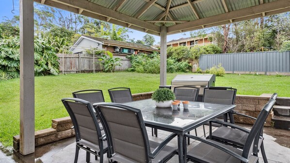 A covered patio with a table and chairs, a small potted plant, and a grill. - Sea Esta at Mollymook (Mollymook Beach)